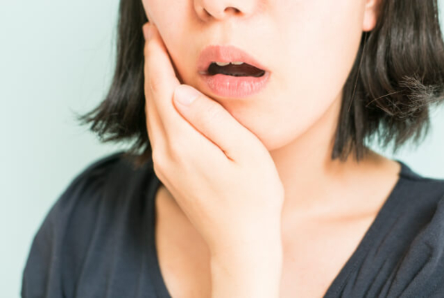 痛みを感じて頬を手で押さえている女性
